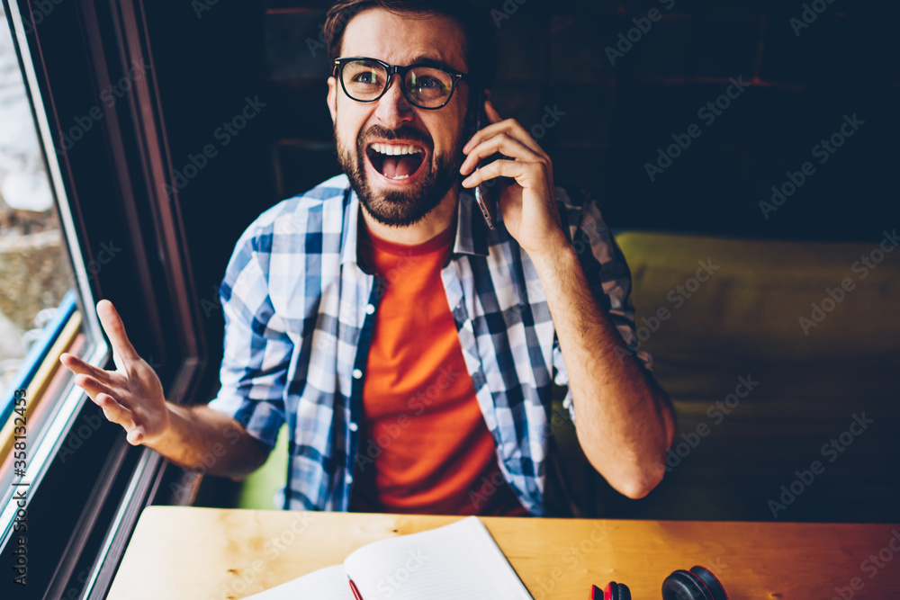 Aufkleber top view of angry bearded hipster guy dressed in casual outfit shouting during phone call on digital