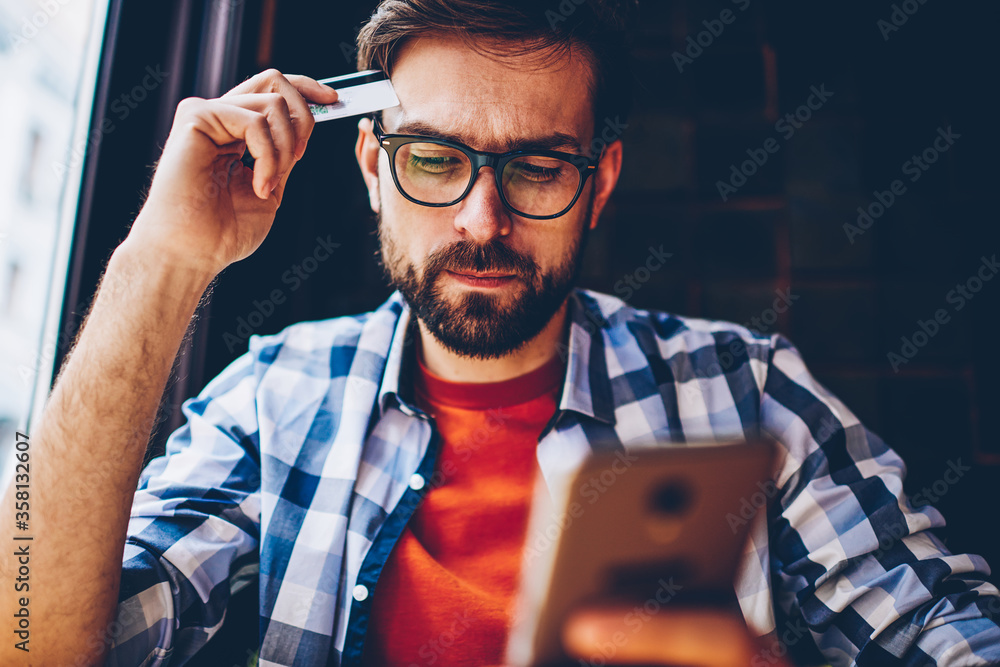 Aufkleber pensive bearded young man in optical eyeglasses for vision correction holding banking card in hands 