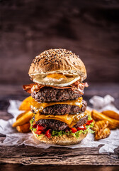 Triple cheeseburger with beef patty, melted cheese, egg and peppers in a rustic wooden environment