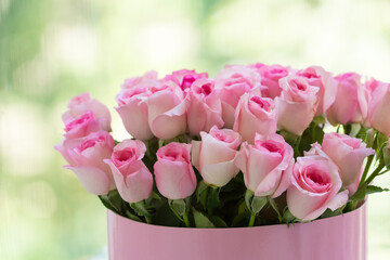 Pink roses bouquet in a box near the window, green bokeh background