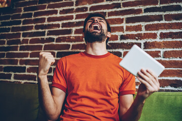 Happy and excited young man rejoicing of victory of sport team during online broadcasting sitting...