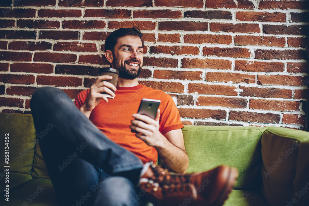 Poster positive bearded bogger with coffee to go in hand smiling and looking away while installing mobile a