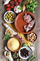 Fototapeta na wymiar Italian dinner table concept with salami, vegetables variety, pasta, polenta, cheese, nuts and herbs. Ingredients for cooking of traditional mediterranean dinner or lunch. Overhead view