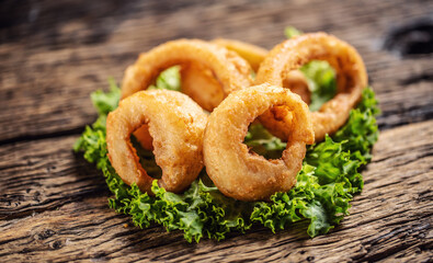 Cripsy onion rings on a lettuce leaf placed on a rustic wood