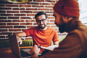 Professional male graphic designer pointing on laptop and explaining task to student.Two hister creative young men collaborating on common project at modern computer connected to 4G internet