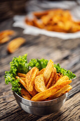 Crispy spiced potato wedges in a metal bowl with salad leaf on dark wood
