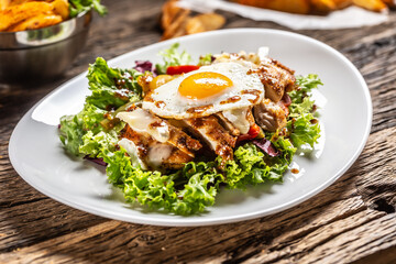 Chicken salad with sunny side up egg and sauce on a white plate and rustic wood