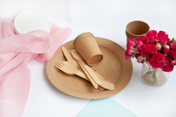 disposable eco dishes made of paper, cardboard, spoon, fork, knife, on a wooden table with red flowers,
