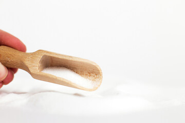 hand with a wooden spoon of salt grain on white background