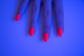 Woman hand with vivid orange manicure in studio neon blue light.