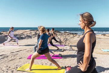 Group of middle-aged men and women doing meditation and a yoga session led by instructor on rocky...