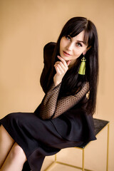 Fototapeta premium a businesswoman in a black dress sits on a chair on a beige background. long beautiful legs