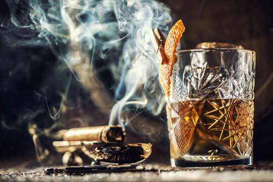 Whisky with no ice in a cup with burning cigar and an old wooden barrel in the background