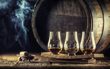 Glencairn whiskey tasting cups on a wooden serving, with a whisky barrel in the dark background and...