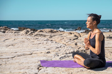 Fototapeta na wymiar woman meditating on a rocky beach in sunny day in lotus pose