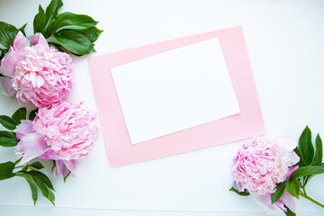 Obraz na płótnie Canvas Creative layout of pink peonies flowers on a white background with a paper card for text. Flat lay, minimalism and nature concept.