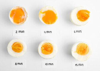 Different cooking time and readiness stages of boiled chicken eggs on white background, flat lay
