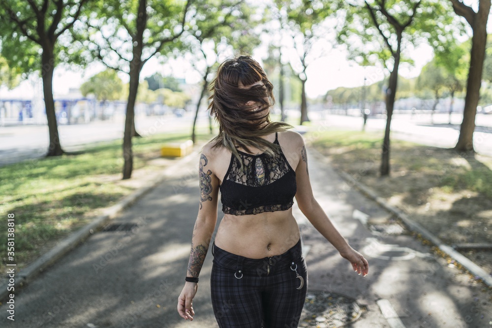 Sticker Young attractive Caucasian female with tattoos standing in the park and making a cute face