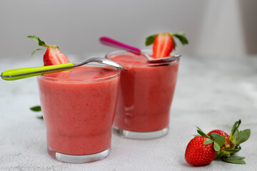 Organic strawberry smoothies in glass cups and ripe strawberries on a gray cement background.