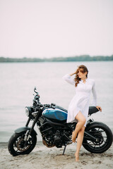 Young woman stands on beach near motorcycle.