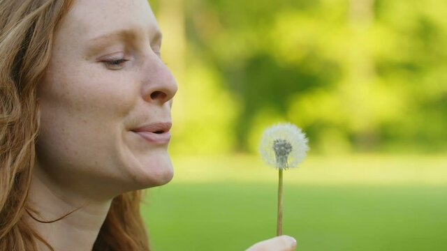 Slow motion closeup shot of a redhead woman blowing a dandelion against the wind.