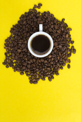 Black coffee in the white cup and coffee beans  on the  yellow background. Copy space. Top view. Location vertical.