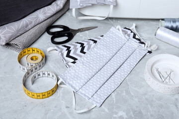Homemade protective masks and sewing accessories on grey marble table