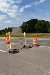 Rear view of traffic barricade and safety barrels, asphalt roadway copy space, blue sky and trees,...