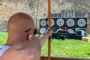 Bold young man aiming to the target with vintage arrow and bow