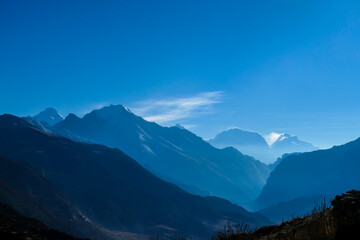 Himalayan chains shrouded in fog, seen from Thorung Phedi, Annapurna Circuit Trek, Nepal. There are multiple mountain chains. Sunbeams breaching through the peaks. Golden hour. Meditation and serenity