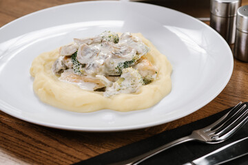 Mashed potatoes with brocoli, mushrooms and sauce on wooden background