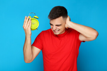 Young man with green alarm clock on blue background