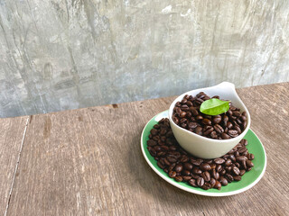 Arabica coffee beans in a cup of beverage and around the cup And with leaves on top are placed on a wooden table, with a background of grunge style coffee break concept. cafe idea.