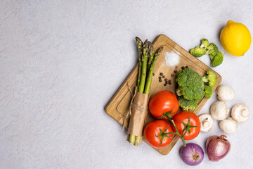 Group of organic fresh vegetables - green asparagus, broccoli, mushrooms on grey background, flat lay. Concept of  healthy vegetarian food, diet and home cooking. Top view, copy space.