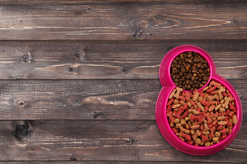 Dry pet food in bowl on brown wooden table