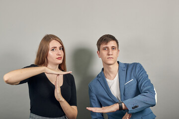 Time out gesture, break, doing t symbol or sign with help of hands. Young attractive couple boyfriend girlfriend two people, dressed black t-shirt, blue jacket, grey background