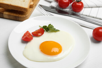 Tasty fried egg with parsley and tomato on white wooden table, closeup