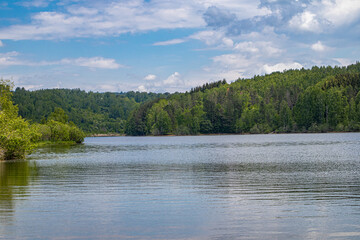 Wavy blue water on a mountain lake and green meadow with forest on a cloudy weather summer day. Travel, tourism, and resort in nature concept. Vlasina lake, Serbia, Europe.