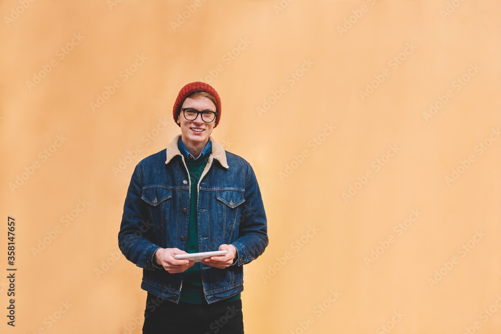 Poster half length portrait of happy hipster blogger dressed in denim jacket smiling at camera while instal