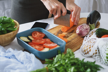 women's hands cut carrots with fluted wavy knife on wooden Board, process of cooking vegetarian dinner