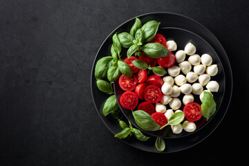 Caprese salad with tomato, mini mozzarella and basil on a black plate.