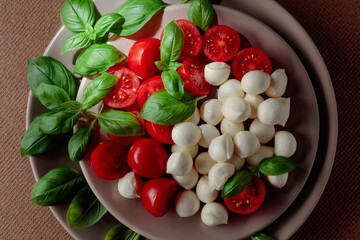 Caprese salad with tomato, mini mozzarella and basil on a brown background.