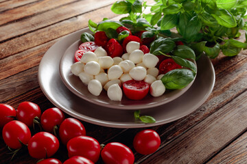 Caprese salad with tomato, mini mozzarella and basil on a old wooden table.