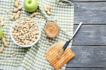 Peanut butter with bread, nuts and apple on grey wooden table