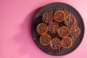 black plate with cups filled with brigadeiro on pink background