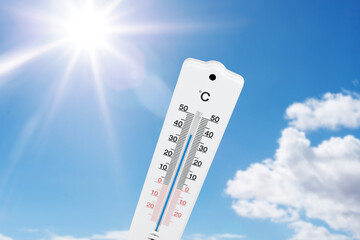 outdoor thermometer indicating high temperatures against blue summer sky and sun