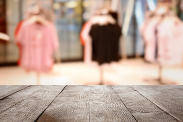 Empty wooden table and blurred view of store with modern clothes