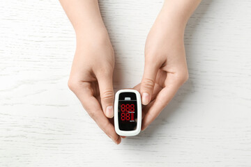 Woman holding fingertip pulse oximeter on white wooden background, top view