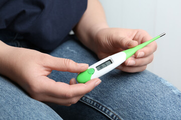Woman with digital thermometer on light background, closeup