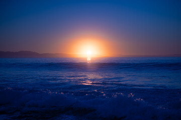 Sunset over ocean with waves crashing into shore